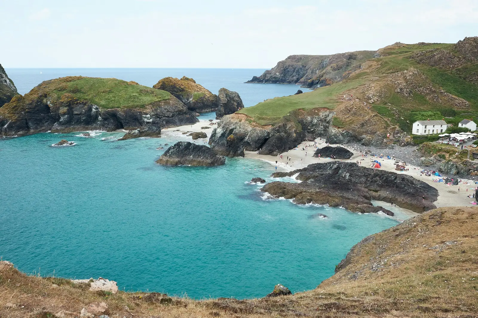 Couple on the clifftop above the turquoise water and rock stacks of Kynance Cove, Cornwall